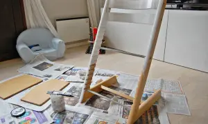 Måla om Stokke stol med vit färg. Trädelar och pensel ligger på tidningspapper.