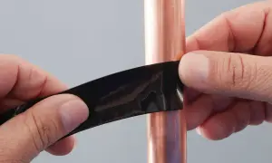 Hände dichten mit schwarzem Klebeband ein kleines Loch in einer Kupferwasserleitung ab.