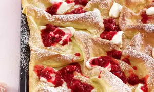 Luftige Pfannkuchen vom Blech, bestäubt mit Puderzucker und garniert mit frischer Himbeersauce und Sahne. Ein Genuss für jeden Anlass!