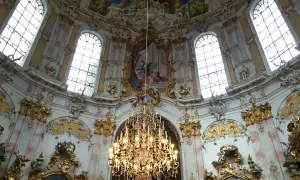 Prunkvoller Kronleuchter unter einer Decke mit Fresken, umgeben von opulenten Verzierungen, die die **Rokoko Architektur** widerspiegeln.