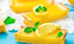 Fette di torta fredda al limone, guarnite con fettine di limone e menta fresca, su un tagliere blu.