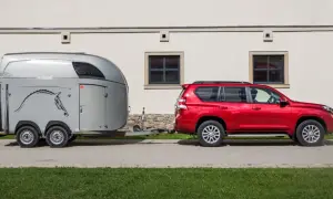 Czerwony SUV ciągnie przyczepę z koniem.