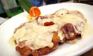 Cotoletta alla bolognese dorata e filante, con prosciutto e formaggio fuso, servita su un piatto bianco.