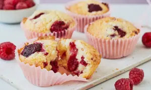 Saftige Himbeer Muffins in rosa Förmchen, einer aufgeschnitten, mit frischen Himbeeren garniert.