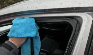 Ręka z niebieską ściereczką czyści uszczelki drzwi samochodu. Dowiedz się, czym smarować uszczelki w samochodzie domowe sposoby, by zapobiec skrzypieniu.