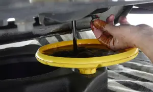 Mano sporca d'olio che tiene il tappo di scarico mentre l'olio scuro cola in una bacinella gialla. Forse c'era troppo olio nel motore.