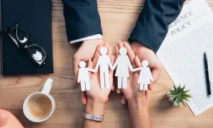 Dłonie trzymające papierową rodzinę na tle dokumentu "Insurance Policy".