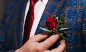 Elegancki, niebieski garnitur w kratę z czerwonym krawatem i subtelnym kwiat w butonierce.