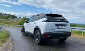 Biały Peugeot 2008 GT na mokrej drodze, z widokiem na krętą trasę i zielone wzgórza.