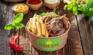 Kebab z frytkami i warzywami w pudełku Kebab King, obok sosów i papryczki chili.