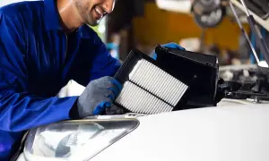 Uśmiechnięty mechanik w niebieskim kombinezonie wymienia filtr powietrza w samochodzie.