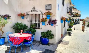Mesa y sillas azules junto a pared blanca adornada con macetas. Un rincón encantador para descubrir qué ver en Mijas.