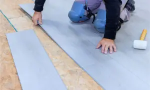 Instalación suelo laminado: un profesional coloca una tabla de suelo laminado gris sobre una base de madera contrachapada.