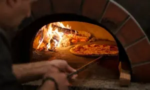 En pizzabagare använder en spade för att flytta en pizza i en vedeldad ugn. Lågorna visar den höga pizzaugn temperatur som krävs för perfekt bakning.