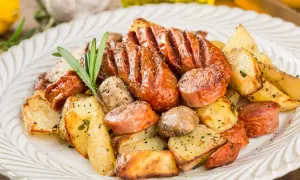 Pyszne dania z piekarnika na obiad: pieczone ziemniaki, kiełbaski i grzyby, doprawione ziołami i pieprzem.
