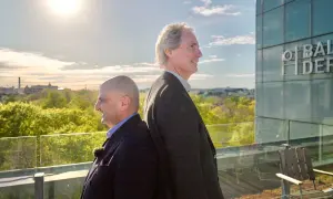 Erik Selin och en kollega står rygg mot rygg på en takterrass med utsikt över en grönskande stad.