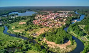 Malownicze miasteczko z czerwonymi dachami rozciąga się nad krętą rzeką, otoczone zielonymi lasami i polami.