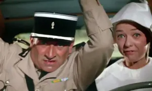 Louis de Funès w filmach, w mundurze żandarma, z przerażoną miną obok kobiety w białym nakryciu głowy.