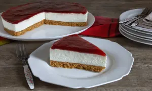Una fetta di cheesecake fredda con copertura rossa su un piatto bianco, accanto a una torta intera.