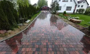 Mokry podjazd z kostki brukowej w odcieniach czerwieni i brązu, prowadzący do domu.