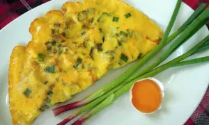 Une omelette à l'aillet, garnie de ciboule verte, est servie sur une assiette blanche avec des tiges d'aillet et un jaune d'œuf.
