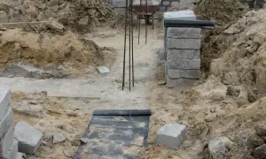 Budowa domu w toku. Widać wykopy, zbrojenie i materiały budowlane. To dopiero początek prac nad fundamentem.