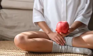 Kobieta w białej koszuli trzyma czerwone jabłko, zastanawiając się, ile kcal ma ten zdrowy owoc.