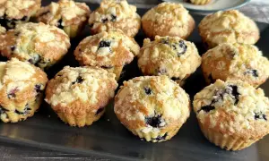 Muffinki z jagodami i kruszonką na ciemnej tacy.