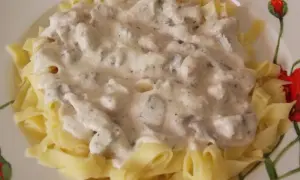 Pyszny makaron z kurczakiem i pieczarkami w kremowym sosie, podany na talerzu z motywem maków.