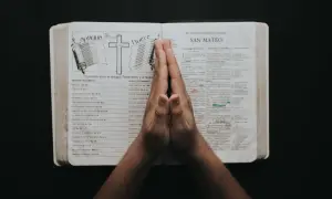 Dłonie złożone w geście modlitwy o prośbę nad otwartą Biblią.