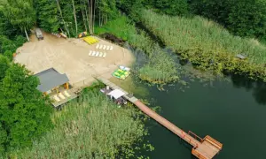 Malowniczy widok na **Pojezierze Brodnickie**: piaszczysta plaża, pomost, łódki i zielone otoczenie.
