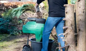 Gartenarbeit: Ein Mann zerkleinert mit einem Häcksler Zweige, um die **Kosten für Heckenentfernung** zu senken.