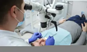 Dentysta pod mikroskopem bada ząb pacjenta. Po leczeniu kanałowym można jeść, ale warto poczekać na znieczulenie.