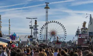Menschenmassen auf dem **Bayern Oktoberfest** mit Riesenrad, Fahrgeschäften und Bierkrügen.