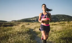 Kobieta w stroju sportowym biegnie ścieżką pośród pól i wzgórz.