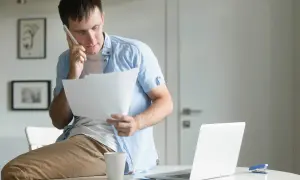 Uomo al telefono con fogli in mano, preoccupato per una busta paga errata in eccesso.