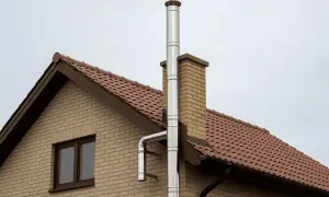 Nowoczesny, metalowy komin na zewnątrz budynku, biegnący wzdłuż ceglanej ściany i dachu pokrytego brązową dachówką.