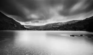 Un photographe paysage capture un lac paisible sous un ciel dramatique, les montagnes se reflétant dans l'eau lisse.