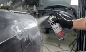 Persona con guante negro aplica imprimación en spray a un coche.