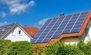 Domy z fotowoltaiką na dachu, zbierające energię słoneczną. Zielone krzewy przed budynkami.