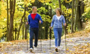 Para spaceruje po jesiennym parku, uprawiając nordic walking. Liście tworzą kolorowy dywan.