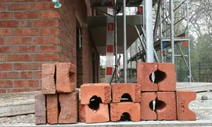 Stos cegieł na budowie. W tle widać fragment czerwonej ściany i rusztowania.