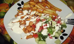 Pyszny kebab na talerzu z chrupiącymi frytkami i świeżą sałatką, polany kremowym sosem.