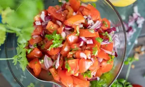 Frischer tomatensalat mit zwiebeln und Petersilie in einer Glasschüssel, garniert mit Koriander.
