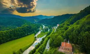 Malownicze **Beskid Sądecki szlaki** wiodą przez zielone doliny, wzdłuż rzeki i lasów, z widokiem na urokliwy kościółek.