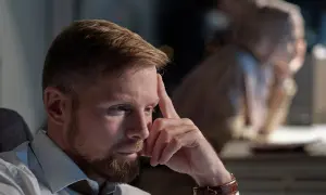 Zamyślony mężczyzna z brodą, odrzucony facet jest niemiły, siedzi przy biurku w nocy, opierając czoło na dłoni.