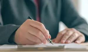 Dłoń w garniturze pisze piórem na dokumencie, co symbolizuje postępowanie egzekucyjne w administracji.
