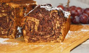 Proste ciasto bananowe z olejem i kakao, z widocznym marmurkowym wzorem. Posypane cukrem pudrem, obok kiść winogron.