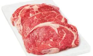 Tre råa, marmorerade entrecôte-biffar på en vit skärbräda, redo för medium rare temp.