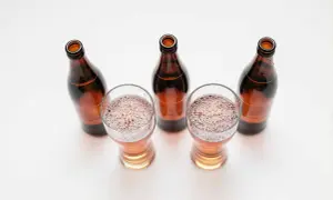 Tre bicchieri di birra con schiuma e quattro bottiglie marroni vuote, una birra andata a male.